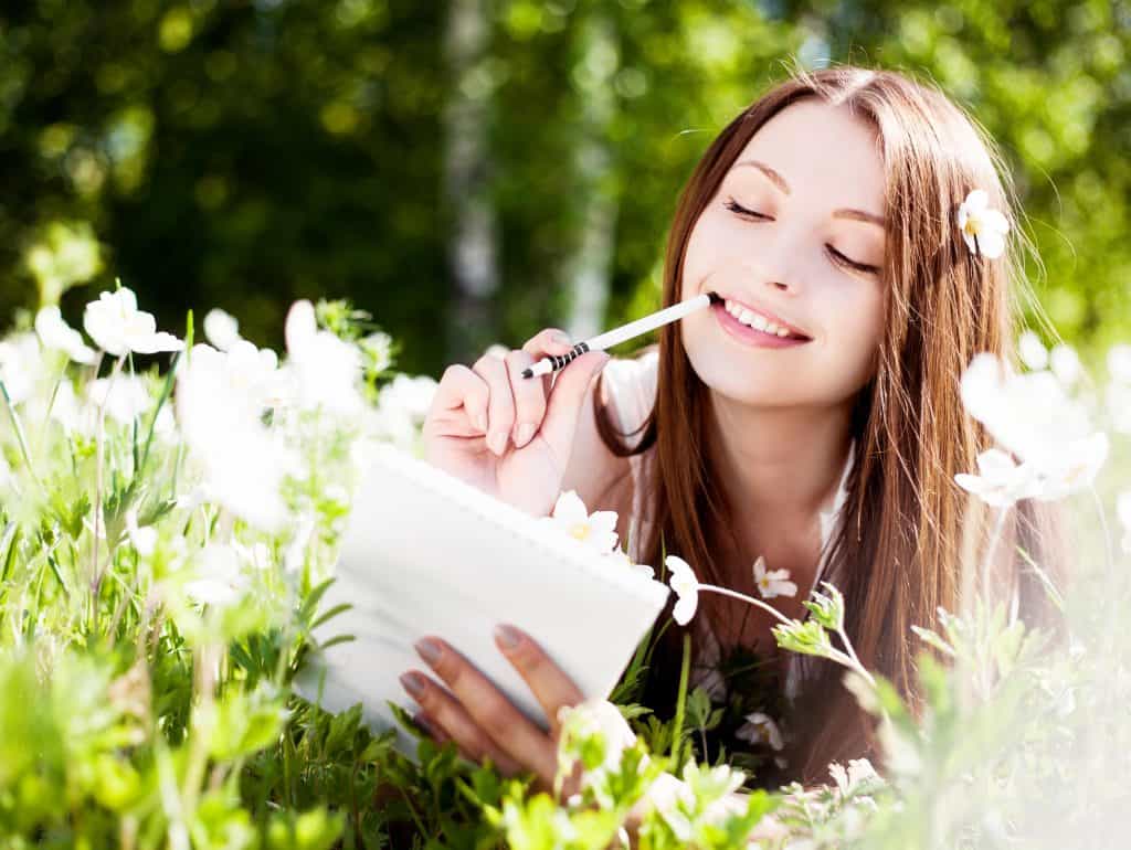 Woman sitting in the garden thinking, holding a pen and paper.
