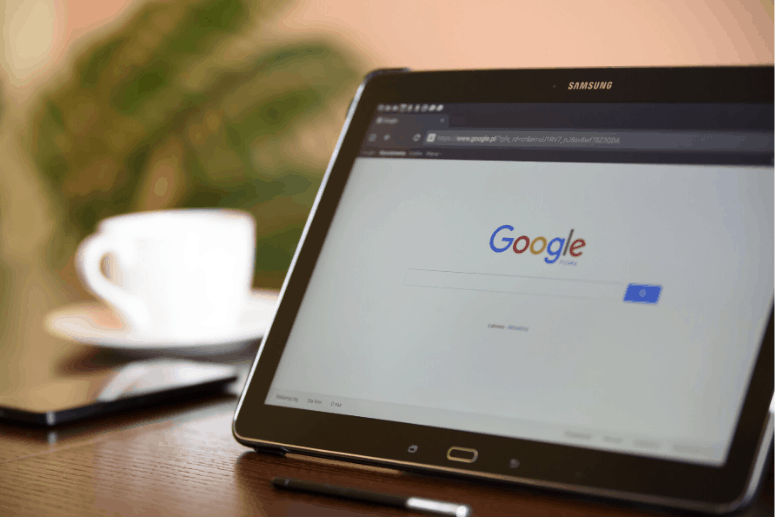 A laptop showing google website and a cup of coffee under the table.