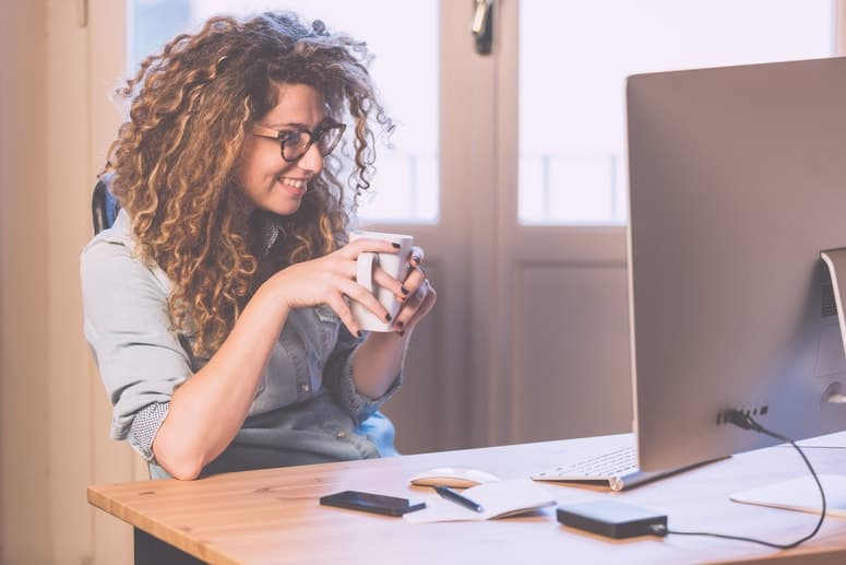Female entrepreneur, sitting on her working desk while drinking a coffee.