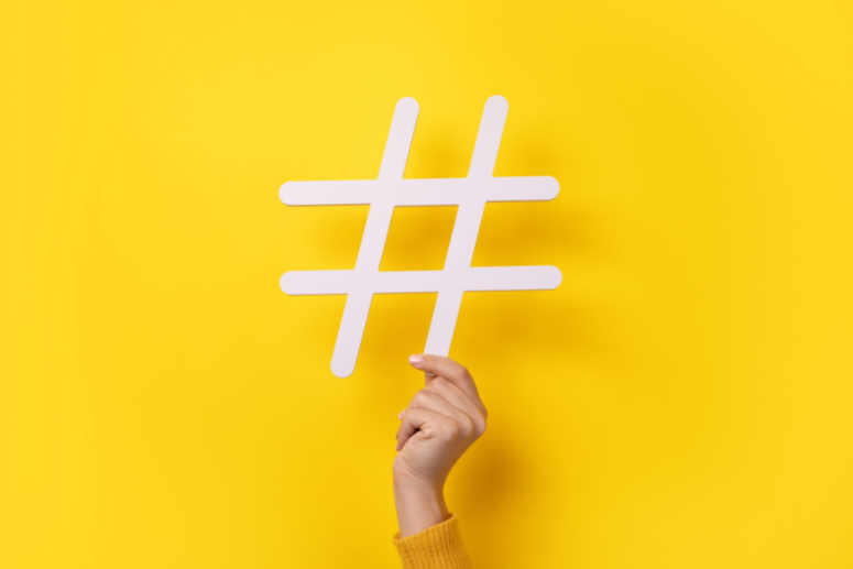 One hand holding a hashtag symbol with yellow background.